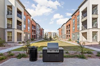 A bbq grill is in the middle of a courtyard surrounded by apartment buildings.